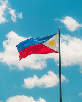 Vibrant Philippine flag waving against a bright blue sky with white clouds. Perfect symbol of national pride.